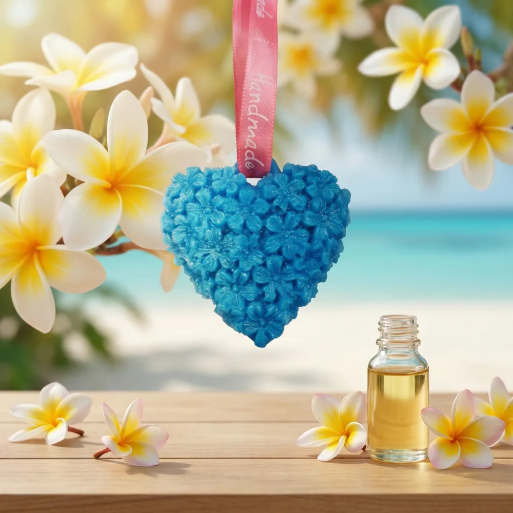 Suspension en cire bleue en forme de cĆur sculptĂ© au parfum de MonoĂŻ, suspendue devant une plage tropicale avec des fleurs de frangipanier et un flacon d'huile parfumĂ©e.