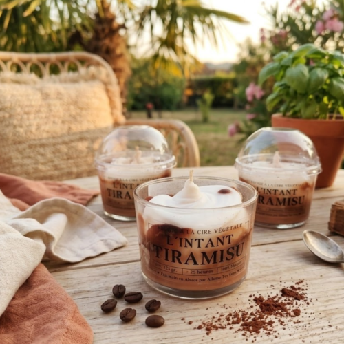Bougie artisanale "L'instant Tiramisu" sur une table de terrasse en bois avec grains de café et décor estival.